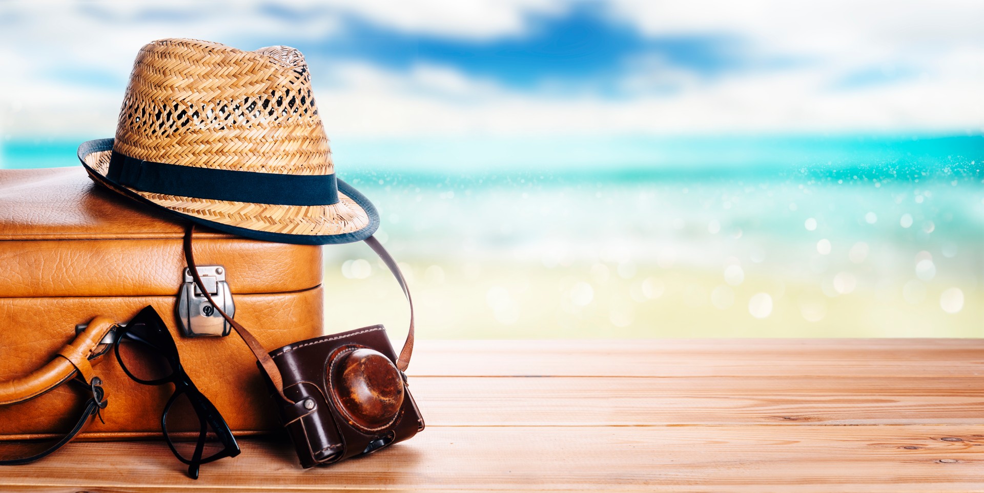 Vintage suitcase, sunglasses and hipster hat wooden deck and blur tropic sea background